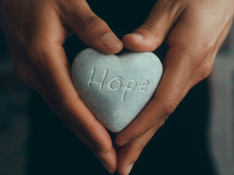 Hands holding stone with 'Hope' written on it